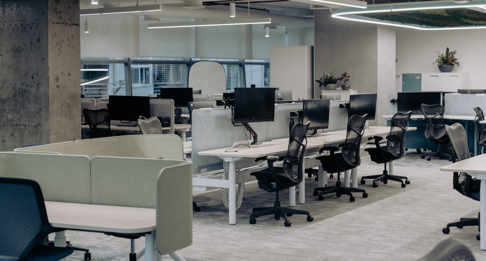 An empty open-plan office — rows of desks with monitors and vacant ergonomic chairs, nobody at them
