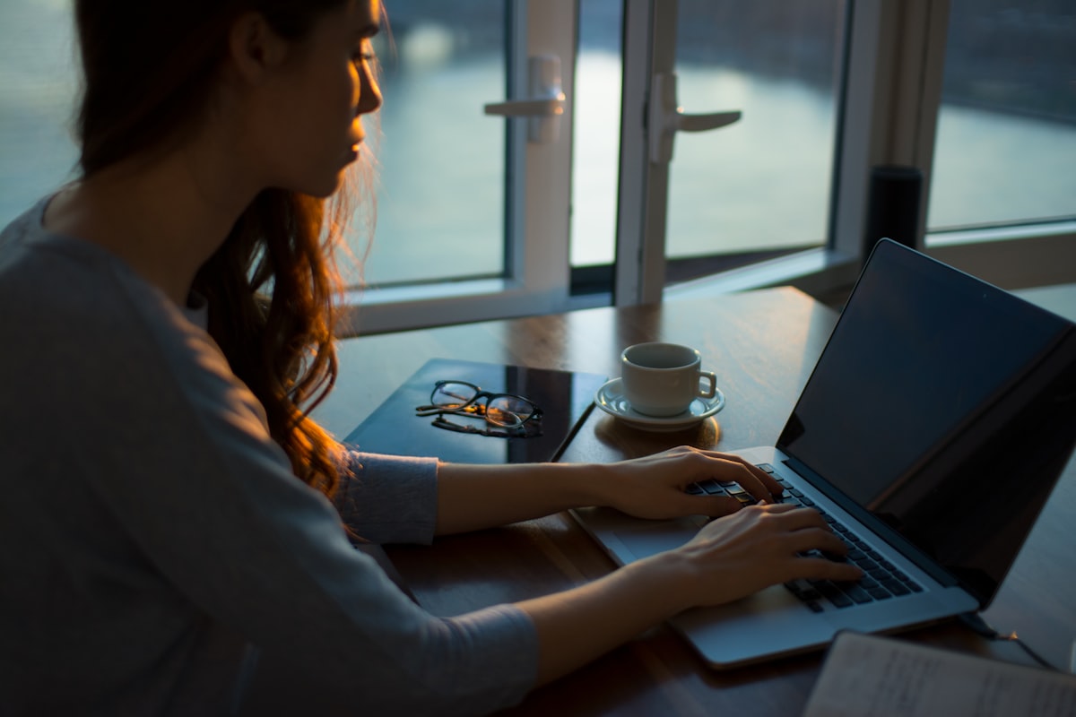 A person working on a laptop by a window with a coffee