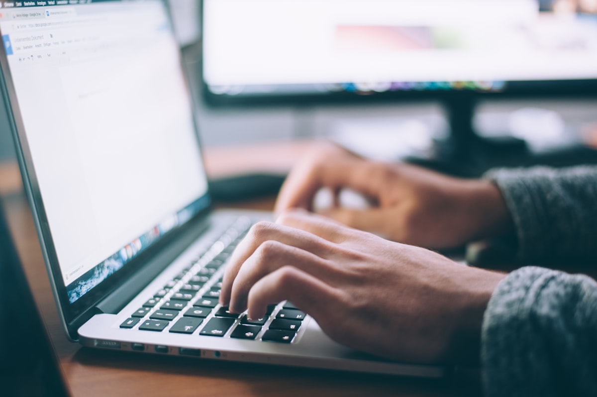 Hands typing on a laptop at a wooden desk